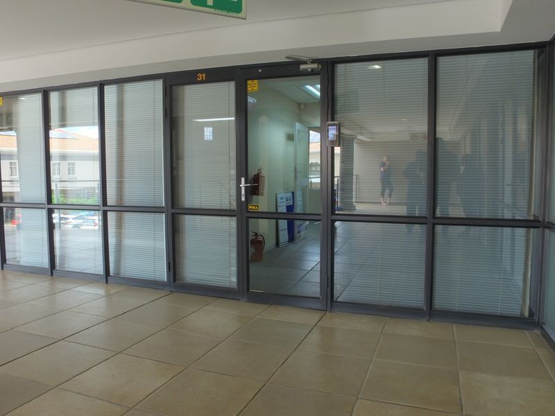 A professional office entrance featuring a modern glass partition wall, aluminum framing, and tiled flooring, providing a clean and accessible workspace entry.