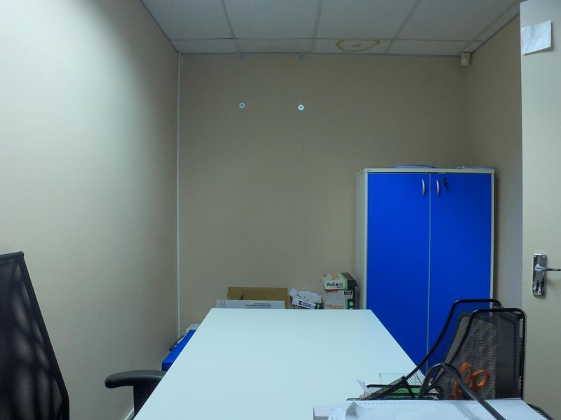 A small office space featuring a suspended ceiling with visible water staining and a built-in blue storage cabinet.