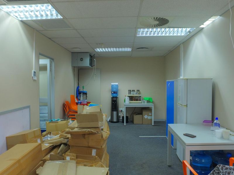 A functional office space featuring a suspended ceiling with recessed lighting, air conditioning, and carpeted flooring, currently used for storage and utility purposes.