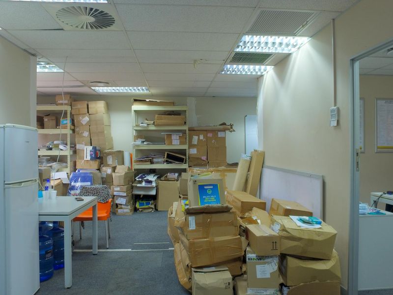 A functional office space featuring a suspended ceiling with integrated lighting and air conditioning, currently utilized for storage with carpeted flooring.