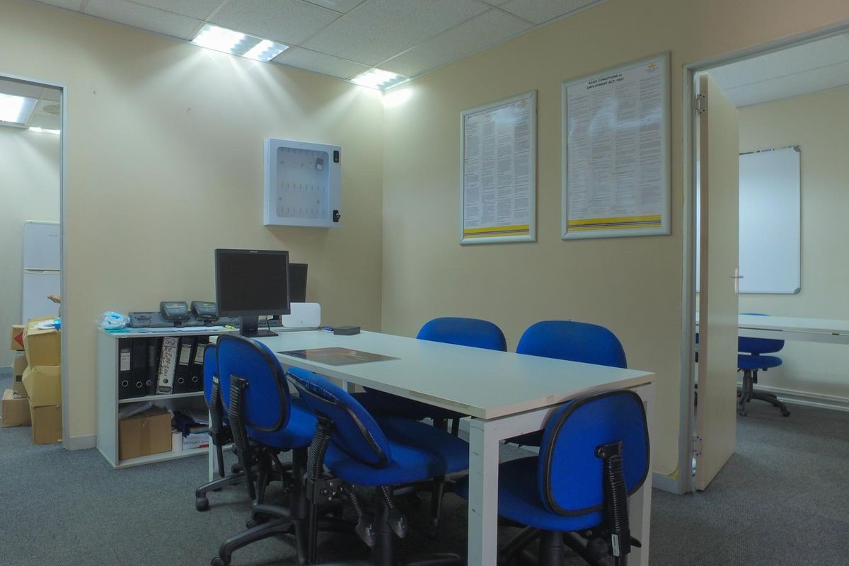 A functional office space featuring carpeted flooring, recessed ceiling lighting, and access to an adjacent workspace.