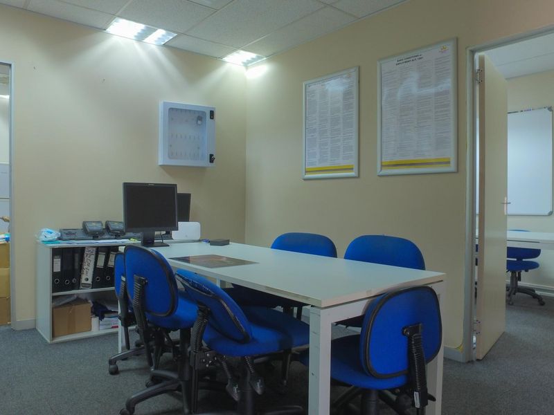 A functional office space featuring carpeted flooring, recessed ceiling lighting, and access to an adjacent workspace.