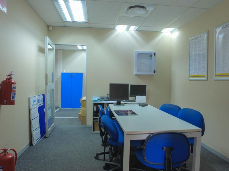 A functional office space featuring carpeted flooring, suspended ceiling with recessed lighting, and wall-mounted safety equipment.