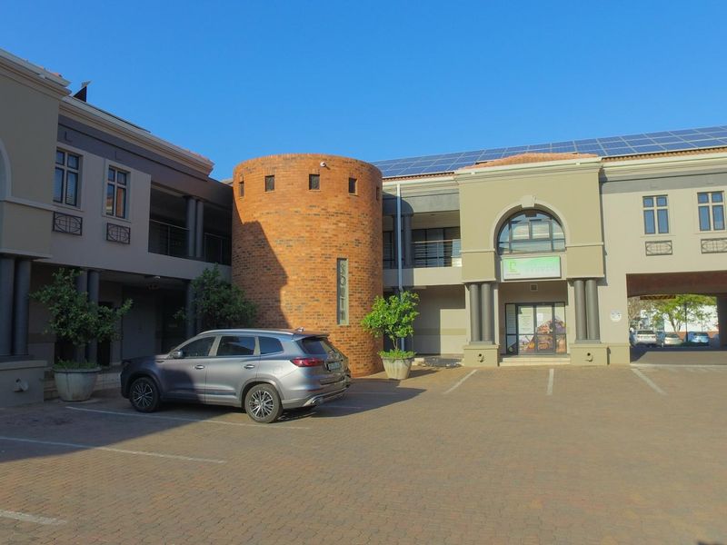 Front view of a modern office complex featuring brick architectural details, paved parking, and roof-mounted solar panels.