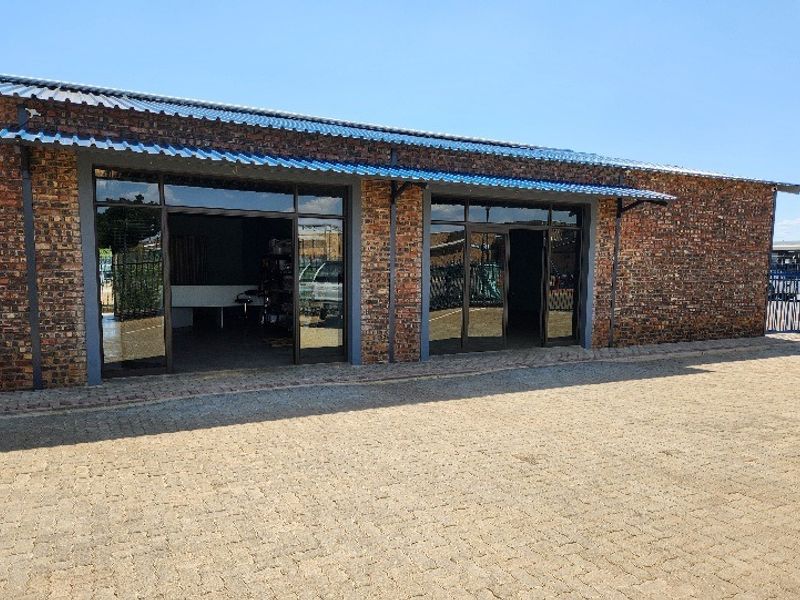 Front exterior view of a commercial office building featuring exposed brickwork, a corrugated metal roof, and large glass sliding door entrances.