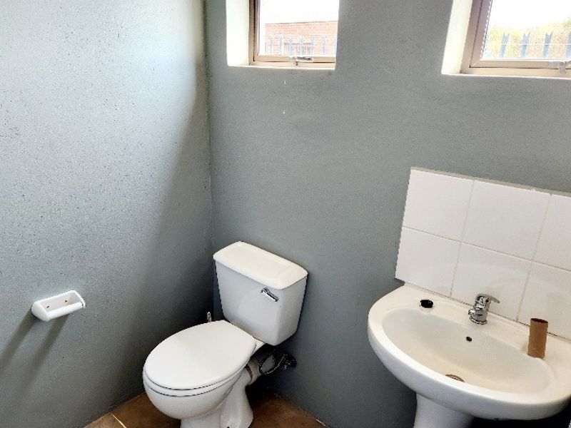 A compact office bathroom featuring a white pedestal basin with tiled splashback and a standard toilet, finished with grey painted walls.