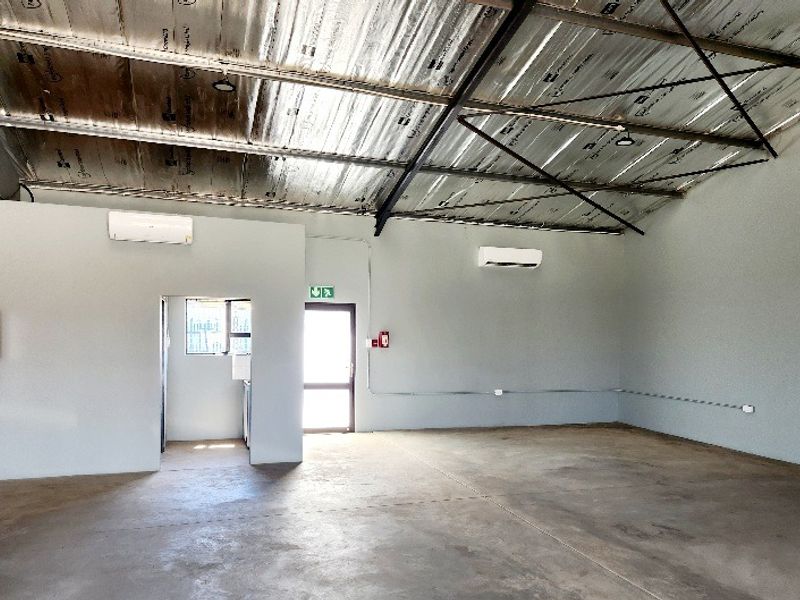 Spacious open-plan office area featuring exposed steel roof trusses, concrete flooring, and dual split-system air conditioning units.