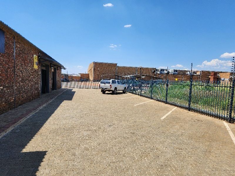 Exterior view of the office property featuring a paved parking area, secure perimeter steel fencing with electric wires, and exposed brick building facade.