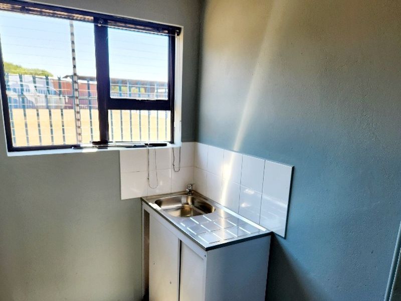 A compact kitchenette area featuring a stainless steel sink, tiled splashback, and built-in cabinetry, suitable for a small office utility space.