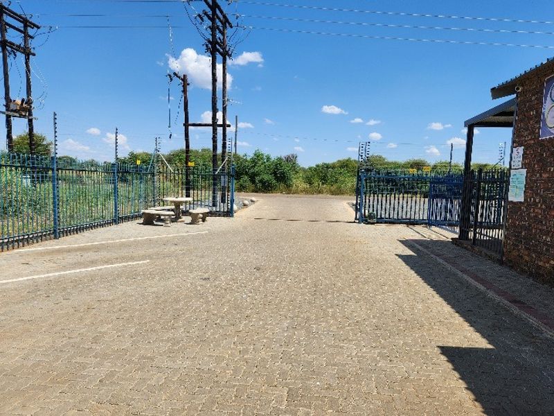 A paved entrance driveway to the office property featuring secure metal gates, electric fencing, and brick boundary walling.