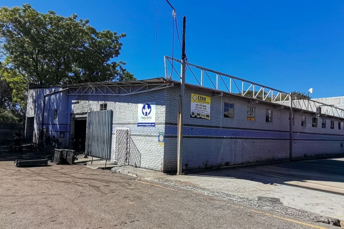 Industrial warehouse exterior featuring brick construction, metal roofing, and a large paved yard area suitable for logistics or manufacturing operations.