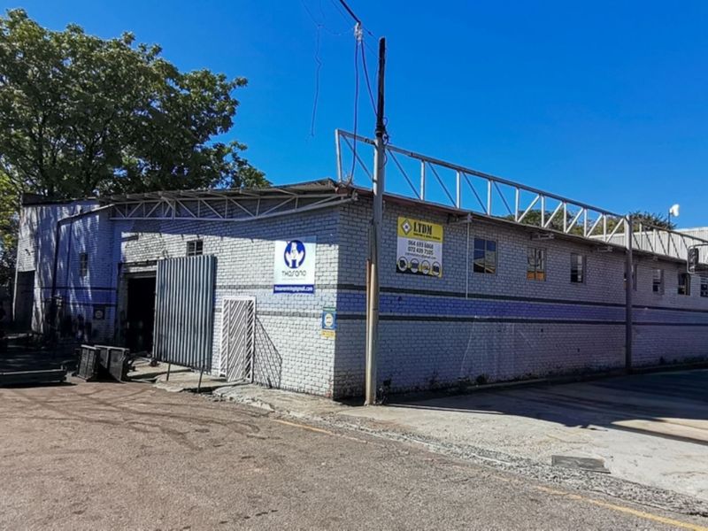 Industrial warehouse exterior featuring brick construction, metal roofing, and a large paved yard area suitable for logistics or manufacturing operations.