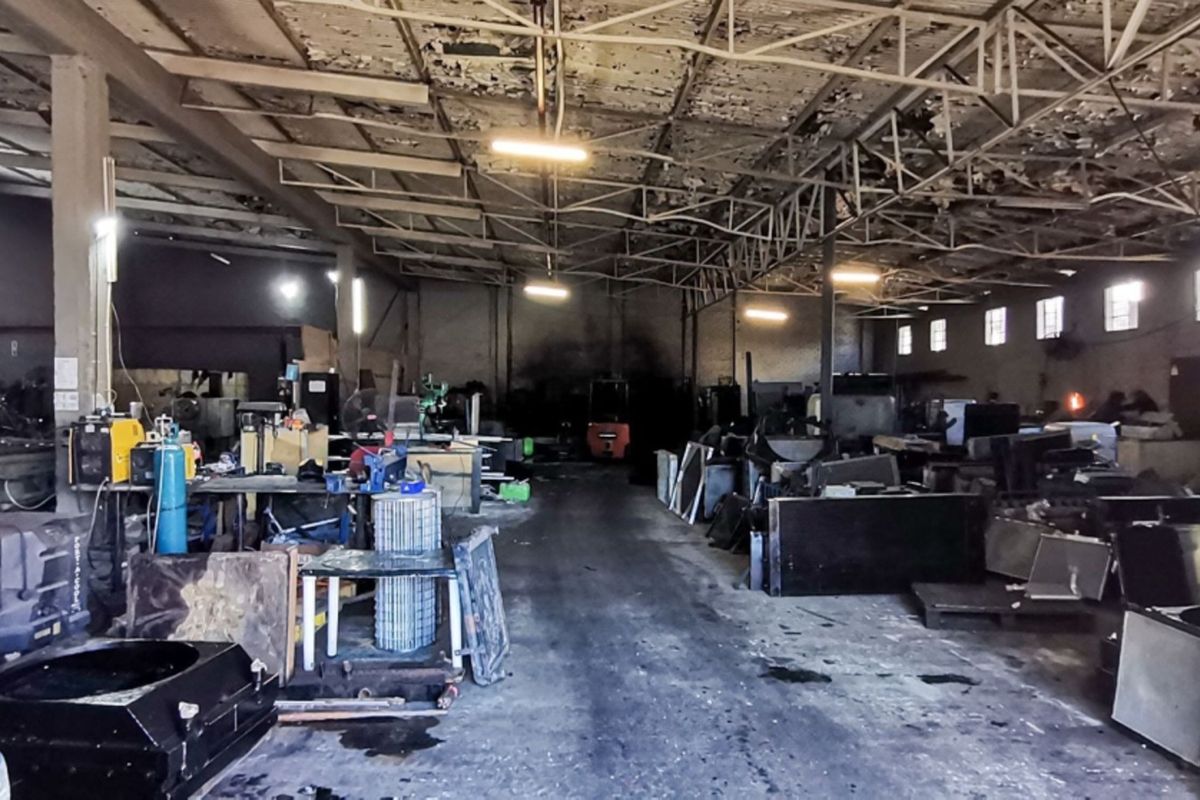 Large industrial warehouse space featuring exposed steel roof trusses, concrete flooring, and masonry walls, currently utilized for industrial operations.