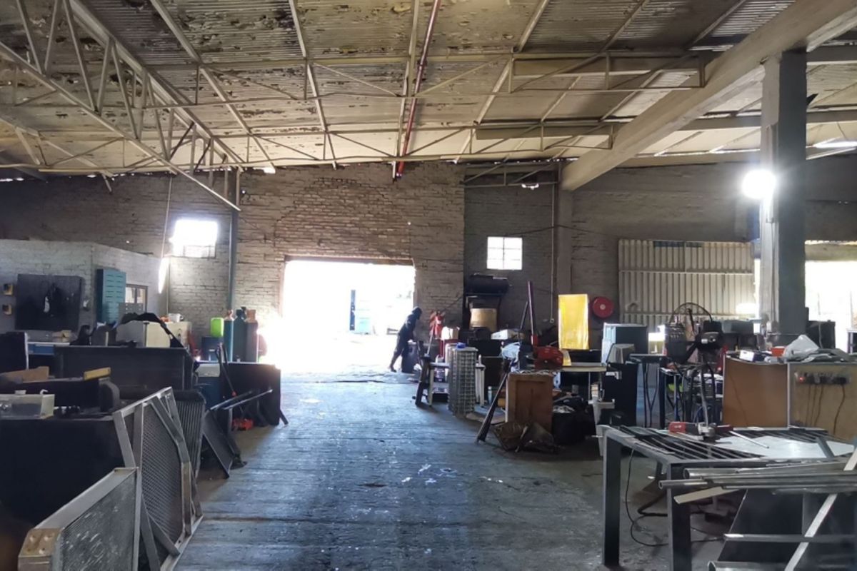 Spacious industrial utility area featuring exposed steel roof trusses, brick walls, and concrete flooring, suitable for workshop or storage operations.