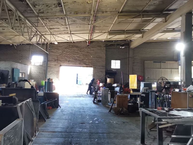 Spacious industrial utility area featuring exposed steel roof trusses, brick walls, and concrete flooring, suitable for workshop or storage operations.