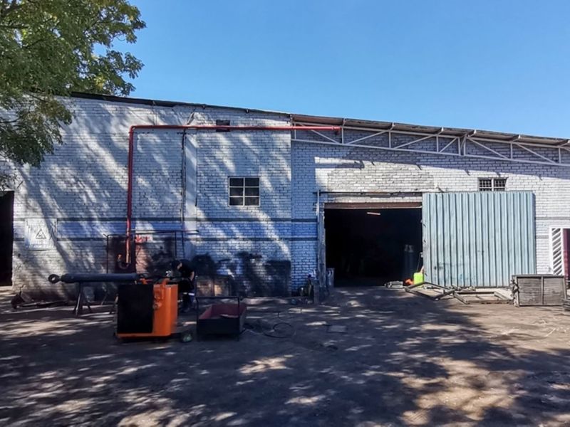 Industrial warehouse exterior featuring a brick facade, large roller door access, and exposed utility piping, suitable for workshop or storage operations.