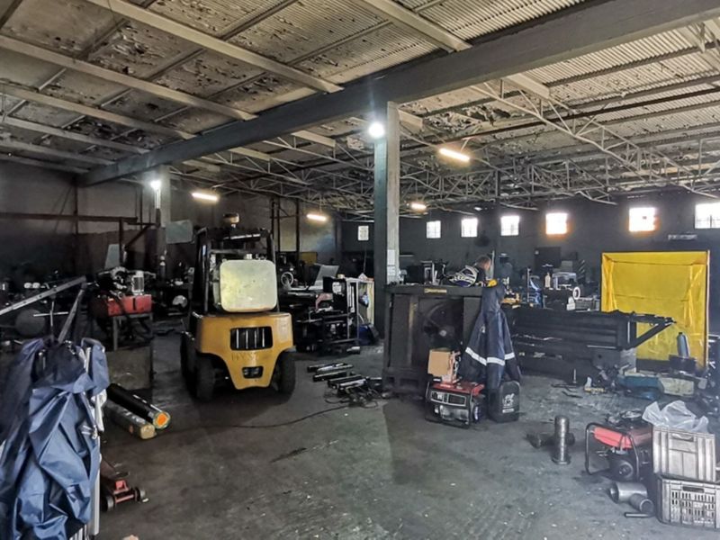 Spacious industrial workshop area featuring exposed steel roof trusses, concrete flooring, and high ceilings, suitable for manufacturing or heavy-duty storage operations.