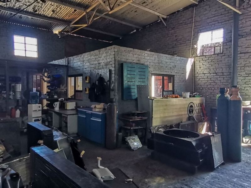 Industrial workshop space featuring exposed brick walls, high corrugated metal roofing, and concrete flooring, suitable for heavy-duty operations or storage.