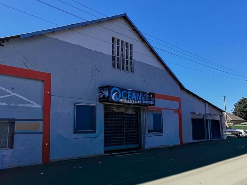 Front elevation of an industrial warehouse building featuring a metal roller shutter entrance, glass block window, and painted brick facade.