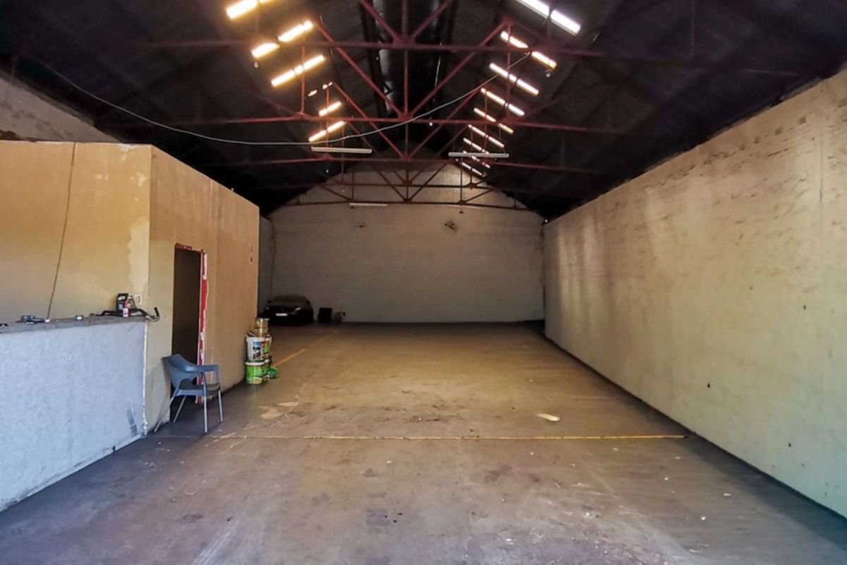 Spacious industrial warehouse unit featuring high exposed steel roof trusses, skylights, and durable concrete flooring, suitable for various commercial or storage applications.