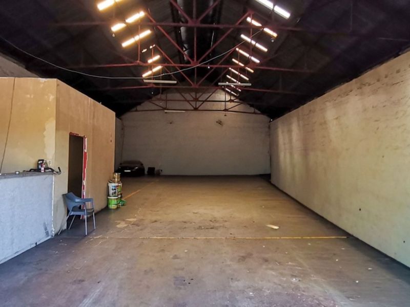 Spacious industrial warehouse unit featuring high exposed steel roof trusses, skylights, and durable concrete flooring, suitable for various commercial or storage applications.