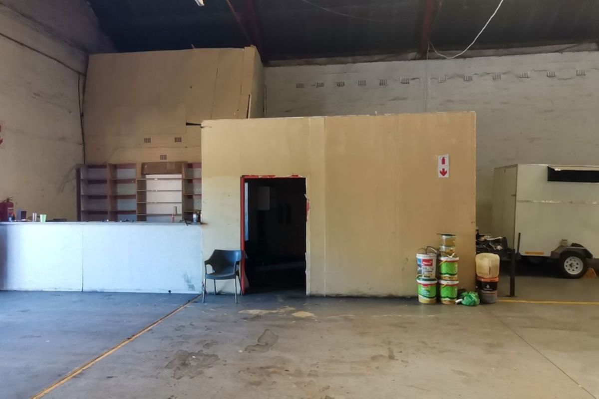 Spacious industrial utility area featuring high ceilings with exposed steel trusses, concrete flooring, and a central partitioned office or storage structure.