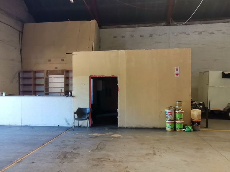 Spacious industrial utility area featuring high ceilings with exposed steel trusses, concrete flooring, and a central partitioned office or storage structure.