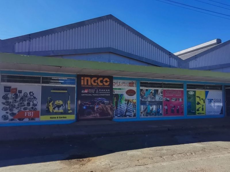 Front elevation of a commercial retail property featuring large display windows, metal roofing, and prominent signage along a concrete sidewalk.