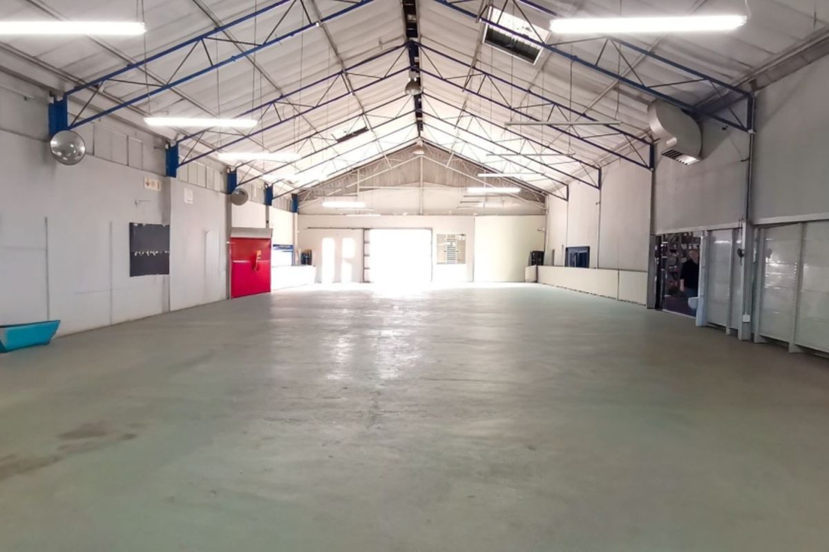 Spacious open-plan warehouse or retail utility space featuring high ceilings with exposed steel trusses, concrete flooring, and ample natural light from skylights.