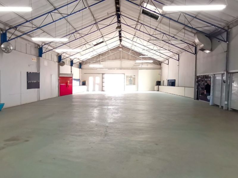 Spacious open-plan warehouse or retail utility space featuring high ceilings with exposed steel trusses, concrete flooring, and ample natural light from skylights.