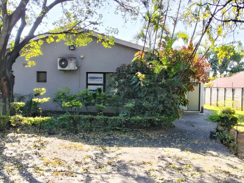 Rear exterior view of the office building featuring a paved driveway, perimeter fencing, and an installed air conditioning unit.