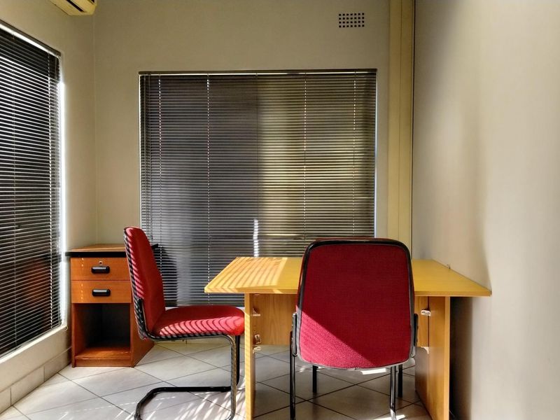 A functional office space featuring tiled flooring, large windows with venetian blinds, and an integrated air conditioning unit.