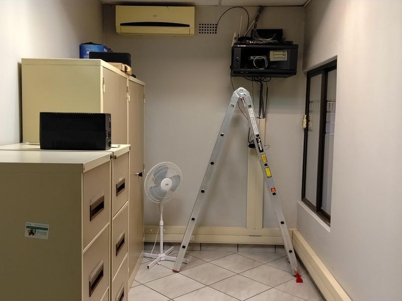 A functional office space featuring tiled flooring, built-in metal storage cabinets, and a wall-mounted air conditioning unit.