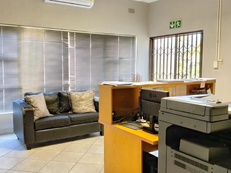 A functional office reception area featuring tiled flooring, built-in reception desk, security gate, and air conditioning unit.