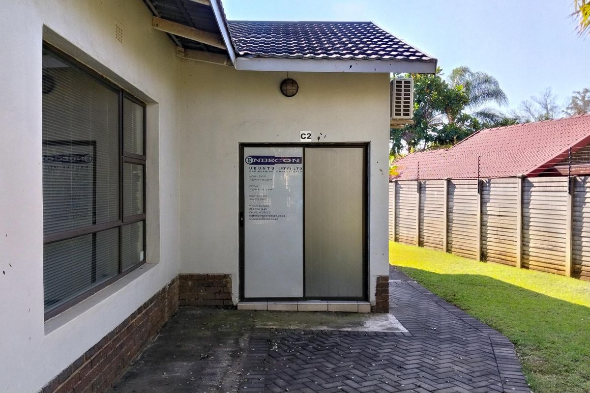 Rear exterior view of the office unit featuring a paved walkway, sliding glass entrance door, and an external air conditioning unit.