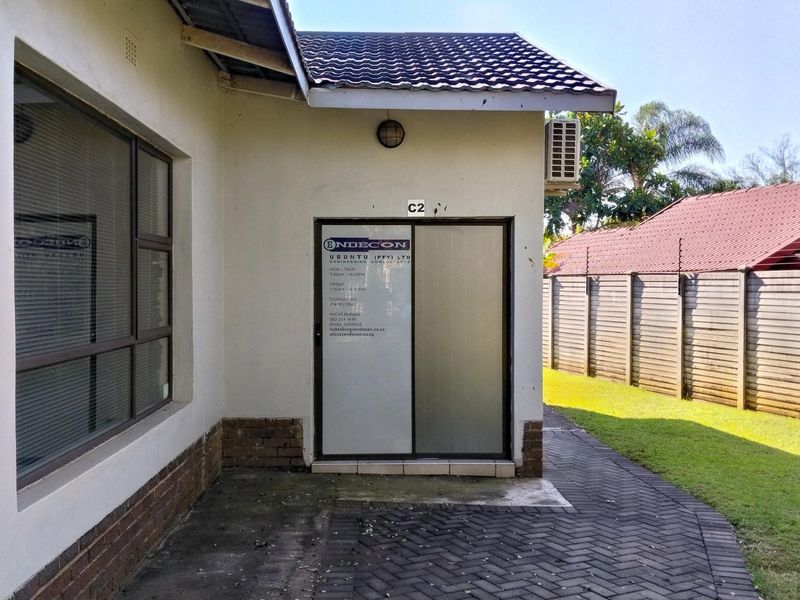Rear exterior view of the office unit featuring a paved walkway, sliding glass entrance door, and an external air conditioning unit.