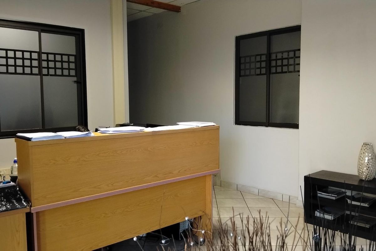 A functional office reception area featuring a built-in wooden desk, tiled flooring, and windows with decorative frosted glass detailing.