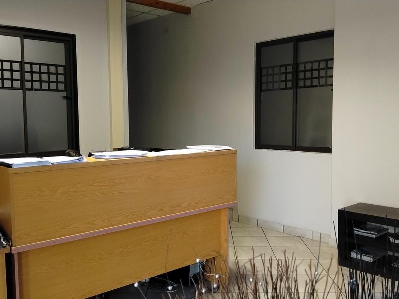 A functional office reception area featuring a built-in wooden desk, tiled flooring, and windows with decorative frosted glass detailing.