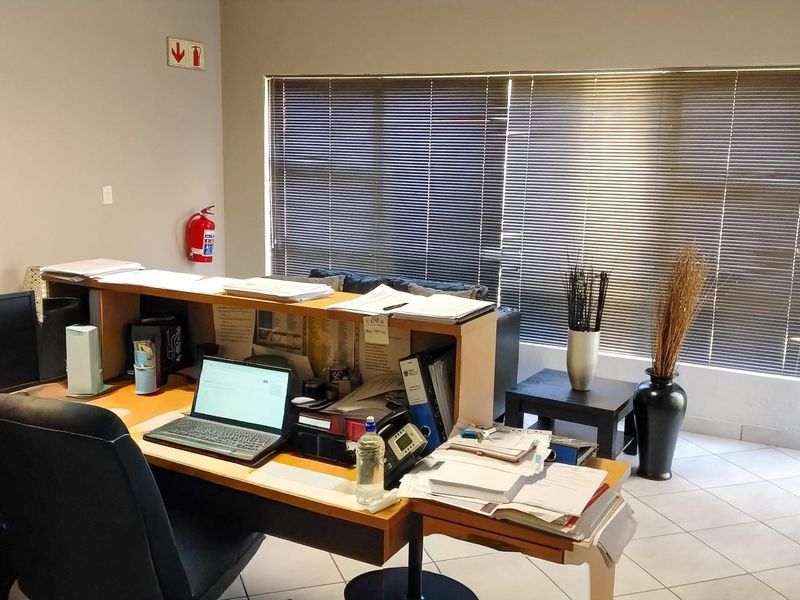 A functional office space featuring tiled flooring, large windows with venetian blinds, and a built-in reception or desk counter.