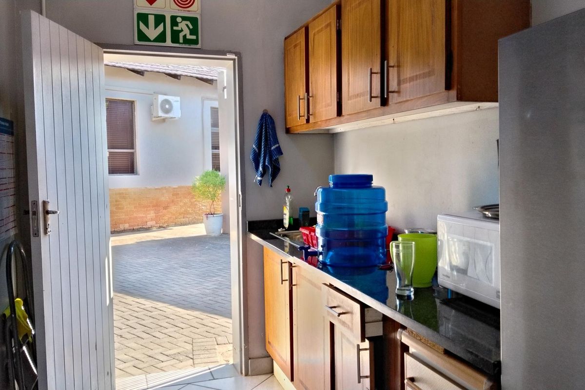 A functional office kitchenette featuring wooden cabinetry, granite countertops, and direct access to an outdoor paved area.