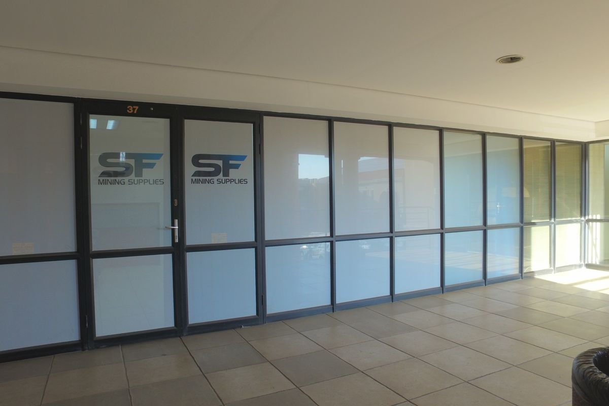 Office entrance area featuring modern aluminium framed glass partitioning, a glass entry door, and neutral tiled flooring.