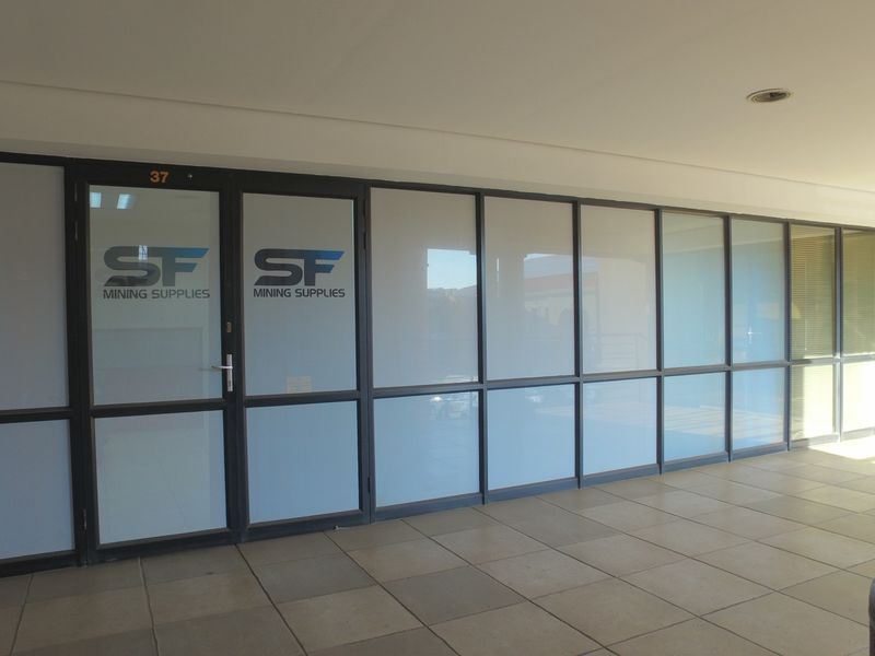 Office entrance area featuring modern aluminium framed glass partitioning, a glass entry door, and neutral tiled flooring.