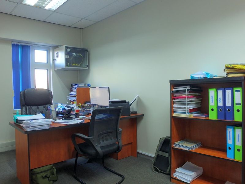 A functional office space featuring a suspended ceiling with recessed lighting, carpeted flooring, and a wall-mounted network cabinet.