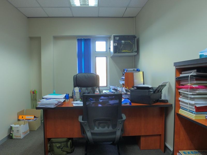 A functional office space featuring a suspended ceiling, recessed lighting, and a wall-mounted network server cabinet.