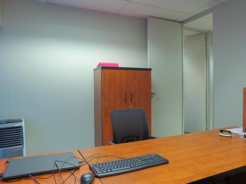 A functional office space featuring neutral walls, a suspended ceiling, and vertical window blinds, providing a professional work environment.