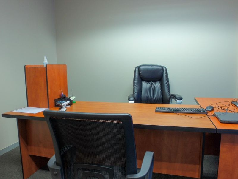 A functional office space featuring neutral wall finishes, carpet flooring, and vertical window blinds, providing a professional environment for work.