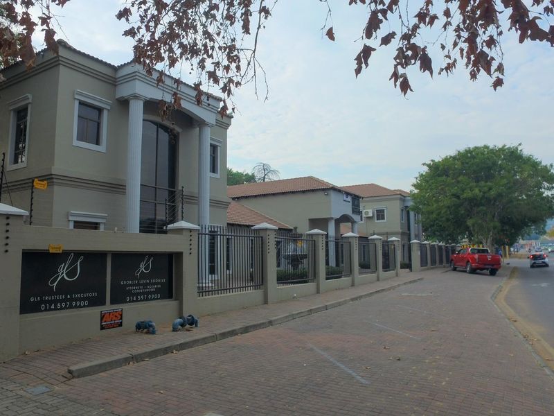 Street-level view of a professional office building featuring a secure perimeter wall, electric fencing, and classic architectural columns.