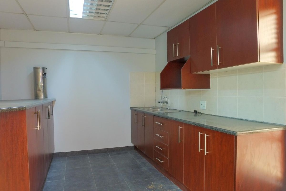 A functional office kitchenette featuring wood-finish cabinetry, stone countertops, a stainless steel sink, and tiled flooring.