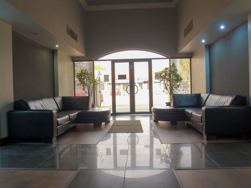 A spacious office building entrance lobby featuring polished tiled flooring, recessed lighting, and large glass doors providing natural light.