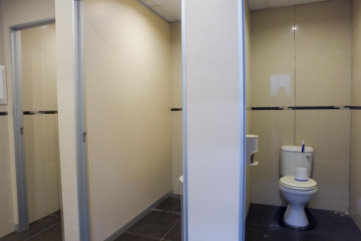 A functional office bathroom featuring multiple toilet cubicles with tiled walls and floors, providing a clean and practical facility for staff and visitors.